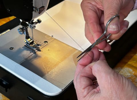 Close-up of hands using scissors to cut thread on a sewing machine, demonstrating precision and skill in tailoring.