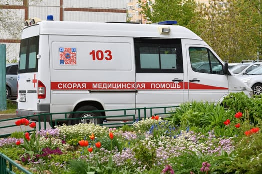Moscow, Russia - May 16. 2024. An ambulance near residential buildings against background of flowers