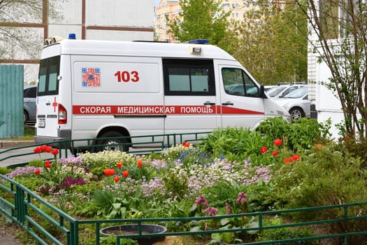 Moscow, Russia - May 16. 2024. An ambulance near residential buildings against background of flowers