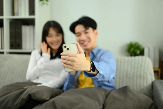 Happy couple relaxing on the sofa and using a smartphone to take a selfie or video call.