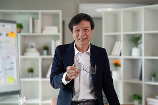 A senior financial advisor joyfully holds his glasses, demonstrating a positive attitude in a modern office environment focused on financial consulting.