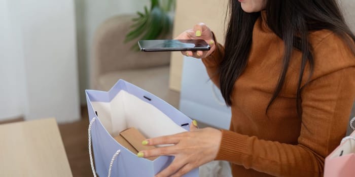 A young woman inspects her shopping bag while using her smartphone, reflecting the modern online shopping experience.