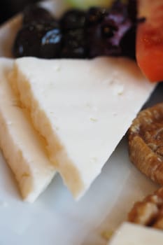 Slices of white cheese placed beside olives and colorful vegetables.