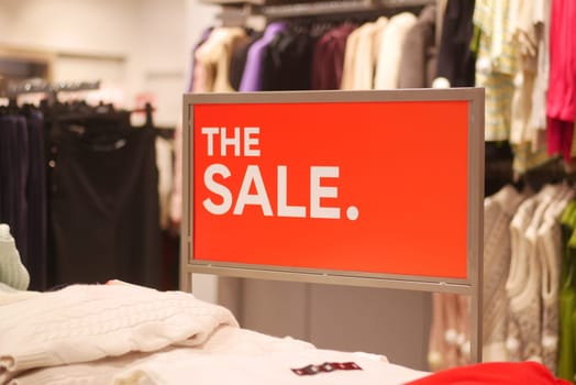 Shoppers are drawn to a vibrant sale sign in a retail space.