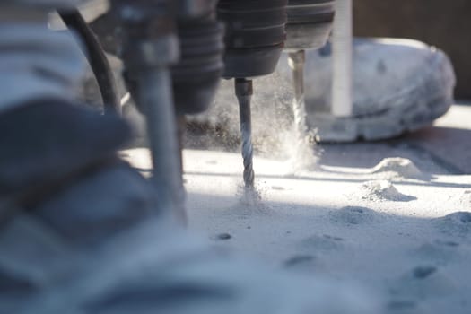 Drill bits are actively cutting into a surface, creating dust.