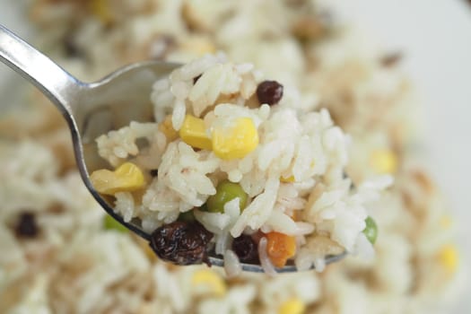 A spoonful of vibrant rice with peas, corn, and dried fruits prepared at home.