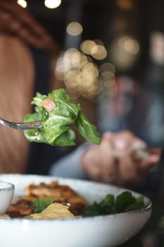 A person enjoys a vibrant salad with greens and toppings in a warm restaurant.