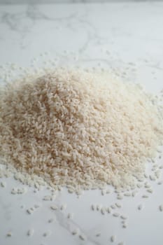 A mound of uncooked white rice is placed on a smooth countertop.