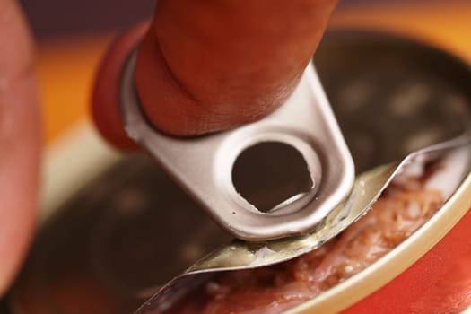 A hand pulls the tab of a canned tuna in a bright kitchen.