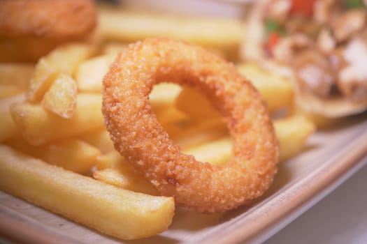 Crispy onion rings accompany golden fries on a wooden plate for lunch.