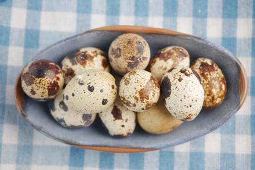 Quail eggs in a wooden bowl on a blue checkered tablecloth.