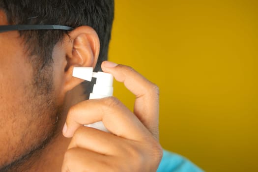 A man is using ear spray for personal hygiene in a bright setting.