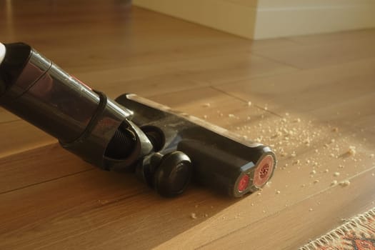 Vacuum cleaner removes dust and debris from a wooden floor indoors.