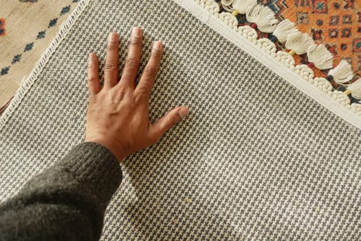 A hand explores the intricate texture of a woven fabric indoors.