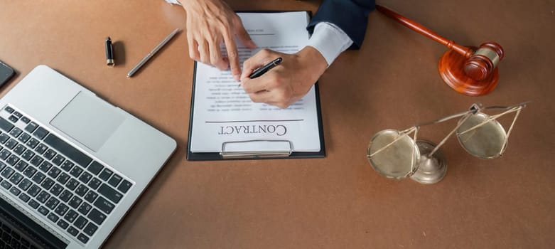 A lawyer signs a contract document while examining legal paperwork at a desk equipped with a laptop and a gavel, emphasizing attention to detail and professionalism.