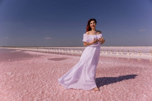 A woman in a white dress stands on a pink salt flat, her hair flowing in the wind. The sky is blue and the salt flat is vast and empty.