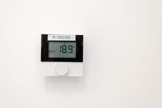 A sleek thermostat showing a temperature of 18.9C on a plain white wall