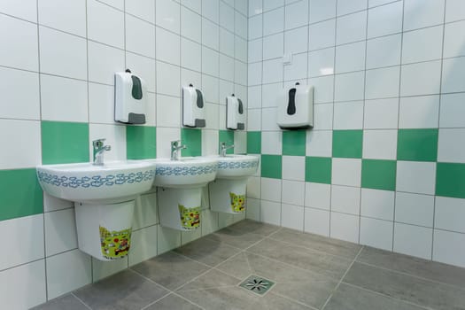 This is a contemporary restroom that showcases stylish sinks alongside vibrant green accents throughout its design