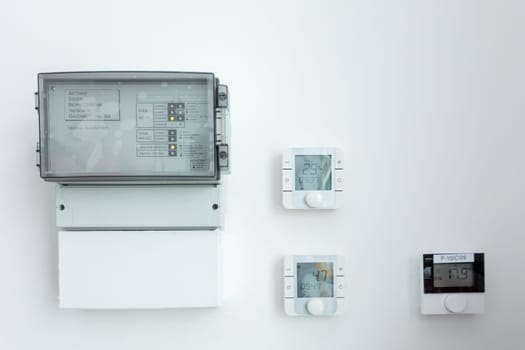 A modern electrical panel along with thermostats is securely mounted on a beautifully clean, minimalist wall