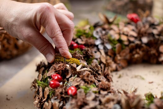 A skilled hand arranging beautiful decorations on a rustic pinecone wreath, perfect for holiday decor