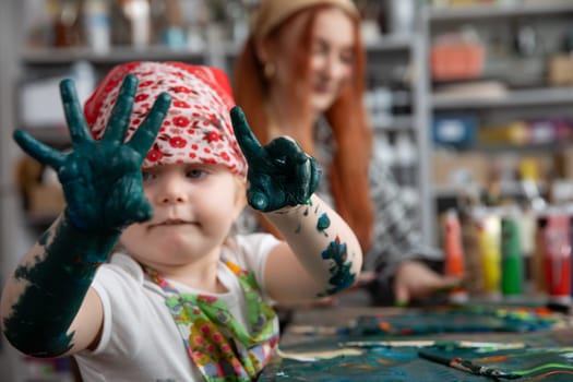 A joyful and delighted child showcases their creativity through the act of painting, hands covered in vibrant colors