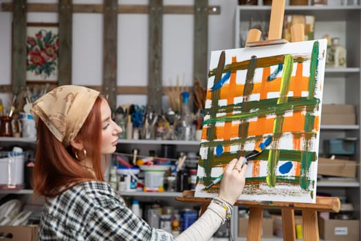 A young woman is fully immersed in the act of painting within her vibrant, colorful studio brimming with art supplies