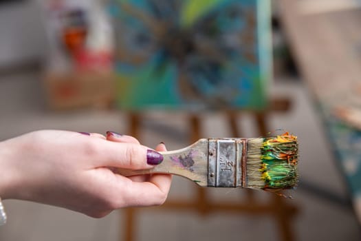 A vibrant paintbrush is firmly held by an artist, showcasing immense creative potential in a bustling studio setting