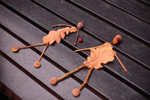 Craft from autumn leaves and acorns. The image of a man and a girl, couple. On dark painted wooden board. Close up