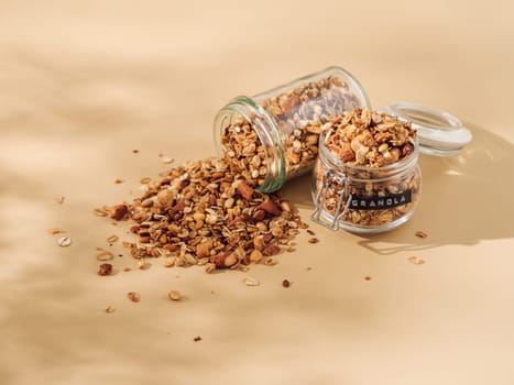 Homemade granola sprinkled of glass jar over pastel beige background. View from above. Aesthetic oat granola, beautiful shadows, champagne yellow background. Healthy breakfast concept. Copy space