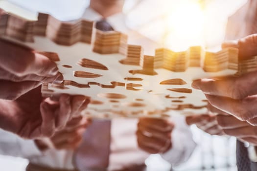 Hand holding wooden gear by businesspeople wearing suit for harmony synergy in office workplace. Bottom view office worker hand make chain of gear into collective unity form.