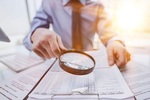 man looking through a magnifying glass to documents notebook.