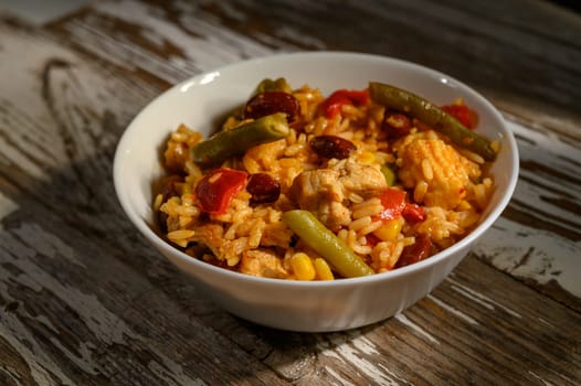 A hearty bowl of rice, chicken, and colorful vegetables awaits on a weathered table under soft afternoon sunlight.