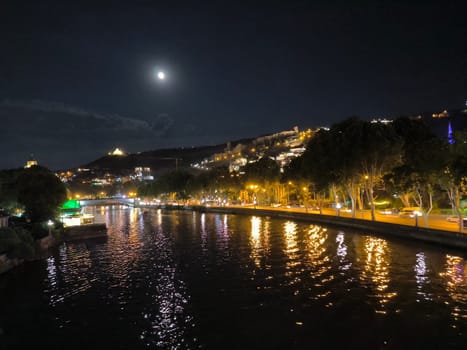 Night light city river landscape background summer town travel tourism black sky moon 17 August 2024 Tbilisi Georgia. High quality photo