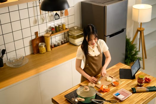 Young Asian woman following a spaghetti recipe on digital tablet while cooking in cozy kitchen.
