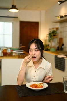 Young woman sitting at a dining table enjoying a plate of homemade spaghetti