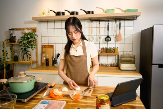 Smiling woman in an apron preparing ingredients for spaghetti in a cozy kitchen.
