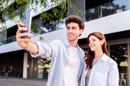 man and a woman are taking a selfie together, the man is holding a cell phone and the woman is smiling, concept of technology and urban lifestyle