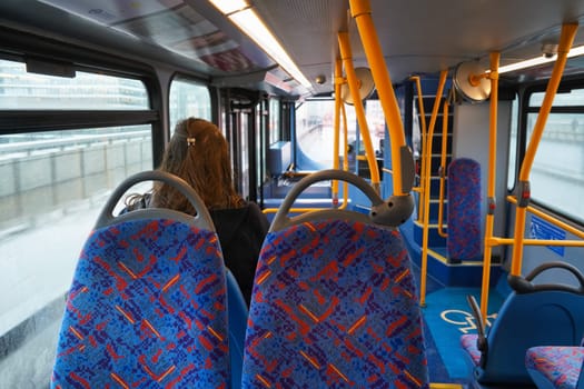 London, United Kingdom - February 01, 2019: Anonymous young female passenger travelling in otherwise empty public transport bus, view from behind, unoccupied seats visible