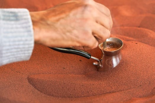 Coffee prepared on street in traditional Arabic way, cezve or ibrik (small Turkish coffe pot) is placed inside red hot sand until liquid boils, detail on local man hand stirring drink
