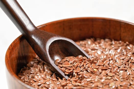 Common flax linseed in small wooden bowl with wooden scoop, closeup detail