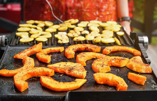 Bright orange butternut squash pieces seasoned with spices grilled on electric grill, blurred potato chips prepared in background