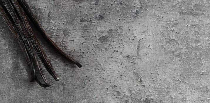 Four bourbon vanilla beans on dark stone like board, view from above, wide banner photo space for text right side
