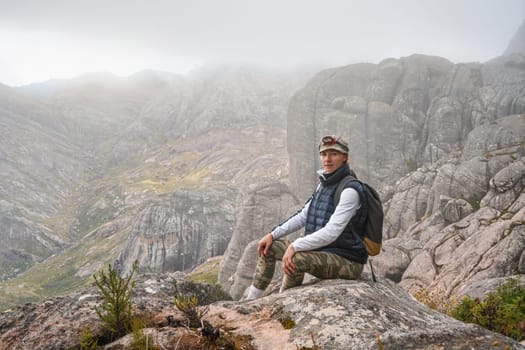 Young woman in sports clothing, headlight torch on her head, sitting on rocks enjoying the scenery of Andringitra national park, large stones massif background, during hike to pic Boby peak