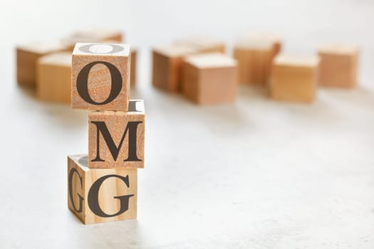 Three wooden cubes with letters OMG (short for Oh my God), on white table, more in background, space for text in right down corner