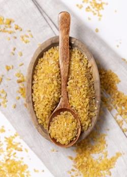 Raw dry uncooked yellow bulgur grain in a wooden spoon on a bowl on cream napkin closeup. Middle Eastern cousine. Organic super food for healthy diet. Ancient alternative cereal. seeds