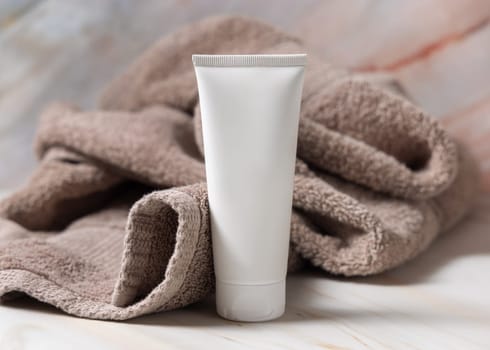 White blank squeeze cream tube on brown towel in bathroom closeup, brand packaging mockup, copy space. Natural handmade cosmetic product for facecare and spa procedures