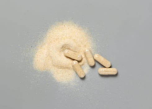 Medical capsules with opened one to show beige powder on grey top view. Preventive medicine and healthcare, taking alternative dietary supplements and vitamins