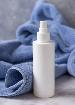White blank spray bottle near blue towel in bathroom closeup, brand packaging mockup. Natural handmade cosmetic product - toner or emulsion for daily face or haircare, copy space