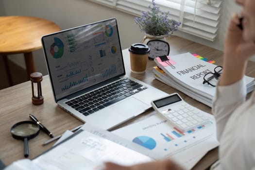A financial analyst reviews data on a laptop, balancing multiple reports and emphasizing efficiency in financial analysis.