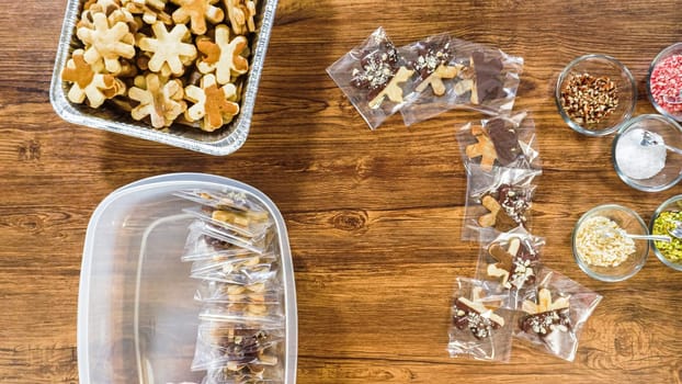 Flat lay. Carefully packaging Christmas cutout cookies, half-dipped in chocolate, sprinkled with crushed nuts, and presented in clear cellophane wrapping.